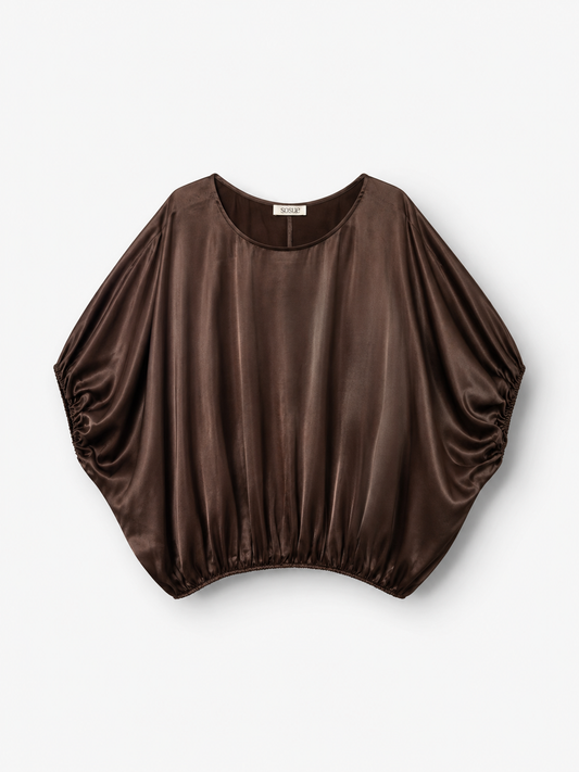 Die Bluse „Cowboy Shiny Braun“ in Dunkelbraun mit glänzender Oberfläche und Fledermausärmeln ist aus LENZING™ ECOVERO™-Viskose gefertigt und verleiht einen eleganten Touch. Diese locker sitzende Damenbluse, hergestellt in Portugal, verfügt über einen gerafften Saum und kommt vor weißem Hintergrund besonders gut zur Geltung.