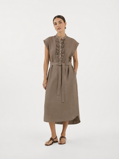 Eine Frau in einem ärmellosen, mit einem Gürtel versehenen Midikleid „Kleid Barcelona Soft Brown“ mit geknöpften Rüschen-Details auf der Vorderseite, die vor einem schlichten weißen Hintergrund steht und braune Sandalen trägt.