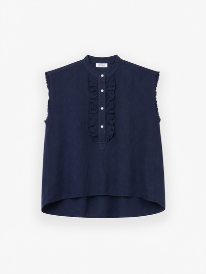 Die „Bluse Barcelona Linen Navy“ ist ein ärmelloses Oberteil in Marineblau mit hohem Kragen, eleganten Rüschen an der Vorderseite, weißen Knöpfen und einem leicht verlängerten hinteren Saum. Es wird vor einem schlichten weißen Hintergrund präsentiert.