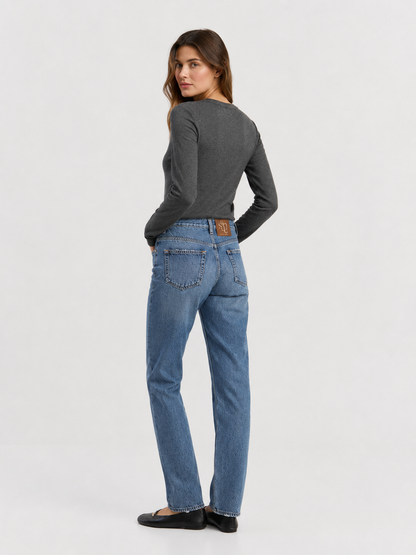 Eine Person steht mit dem Rücken zur Kamera vor einem hellen Hintergrund und trägt das dunkle Langarm-Rippshirt aus Kaschmir, blaue Jeans und schwarze Schuhe. Das Langarm-Rippshirt aus Kaschmir, das fachmännisch gefertigt und in Portugal hergestellt wurde, kommt besonders gut zur Geltung, während die Person über die Schulter in Richtung Kamera blickt.