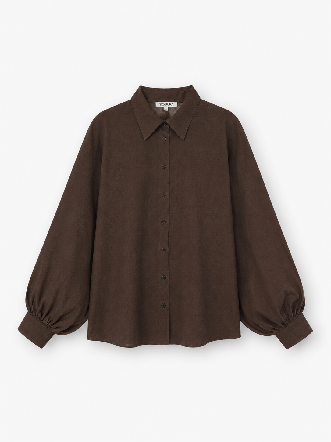 Die Bluse „Antonia Slim Espresso“ ist eine dunkelbraune, langärmelige Bluse mit Knopfleiste, spitzem Kragen und voluminösen Ballonärmeln, die an den Manschetten gerafft sind. Sie ist aus hochwertiger Baumwolle gefertigt und wird vor einem weißen Hintergrund präsentiert. Diese elegante Bluse wird in Portugal in meisterhafter Handarbeit hergestellt.