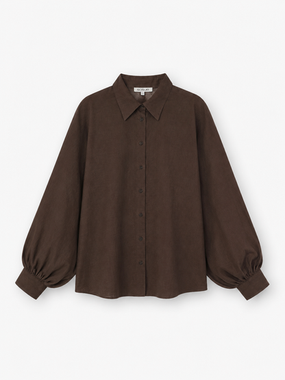 Die Bluse „Antonia Slim Espresso“ ist eine dunkelbraune, langärmelige Bluse mit Knopfleiste, spitzem Kragen und voluminösen Ballonärmeln, die an den Manschetten gerafft sind. Sie ist aus hochwertiger Baumwolle gefertigt und wird vor einem weißen Hintergrund präsentiert. Diese elegante Bluse wird in Portugal in meisterhafter Handarbeit hergestellt.