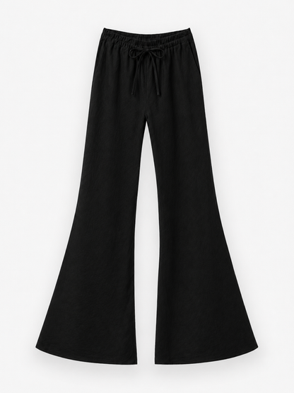 Die Hose „Joana Black“ ist eine weit geschnittene Schlaghose aus 100 % Leinen in einem schicken Schwarzton, die mit einem elastischen Bund und einem Kordelzug für hohen Tragekomfort ausgestattet ist. Diese schwarze Leinenhose bietet atmungsaktive Leichtigkeit, ideal für Sommertage, und wird elegant vor einem weißen Hintergrund präsentiert.