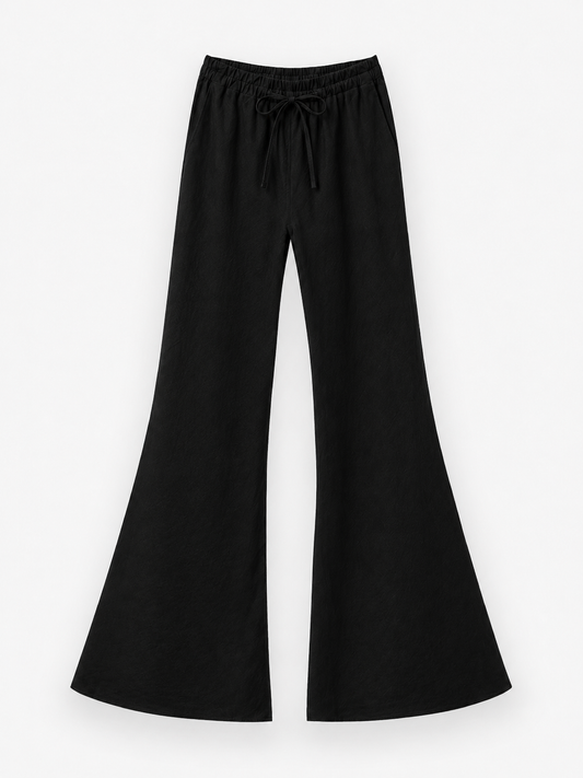 Die Hose „Joana Black“ ist eine weit geschnittene Schlaghose aus 100 % Leinen in einem schicken Schwarzton, die mit einem elastischen Bund und einem Kordelzug für hohen Tragekomfort ausgestattet ist. Diese schwarze Leinenhose bietet atmungsaktive Leichtigkeit, ideal für Sommertage, und wird elegant vor einem weißen Hintergrund präsentiert.