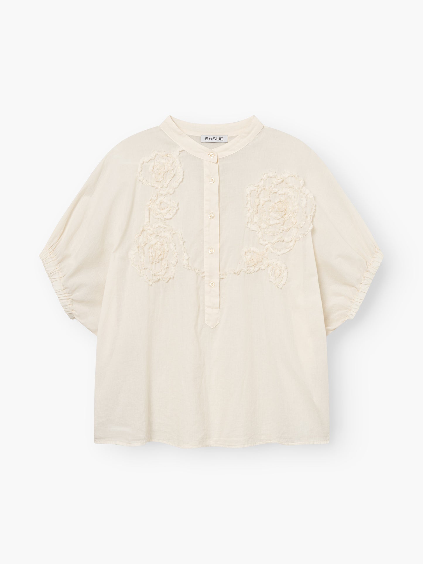 Die Cowboy Crafted Panna ist eine locker sitzende, cremefarbene Bluse mit kurzen Ärmeln, einem Rundkragen, einer teilweisen Knopfleiste und einer strukturierten Blumenstickerei auf der Vorderseite.