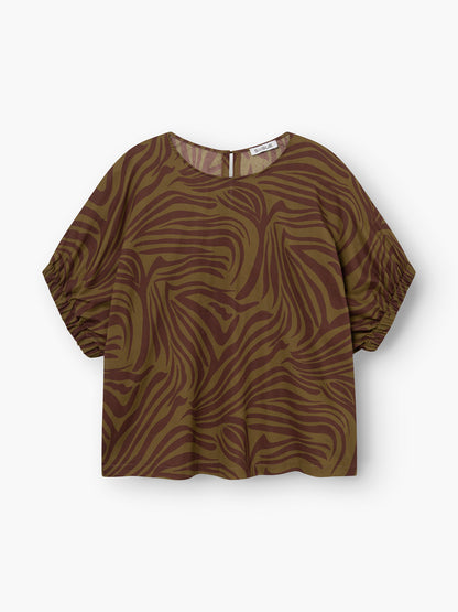 Das Bluse Cowboy Zebra Olive ist ein kurzärmeliges, locker sitzendes Oberteil mit braunem und olivfarbenem Zebramuster, leicht gerafften Ärmeln, Rundhalsausschnitt mit Schlüsselloch im Rücken, gefertigt aus weichem Baumwoll-Voile für hohen Tragekomfort.