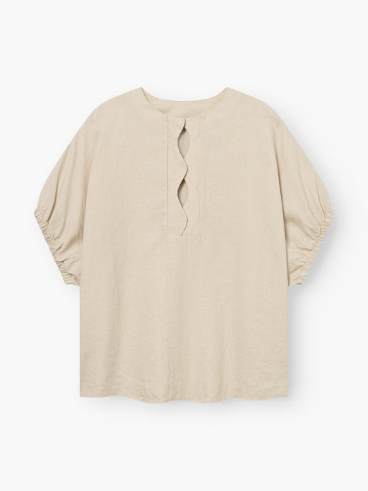 Die Bluse Cowboy Wave Linen Beige ist eine locker sitzende Bluse aus beigem Leinen mit ellenbogenlangen, leicht gepufften Ärmeln und einem markanten Schlitz mit Wellendetail am vorderen Halsausschnitt.
