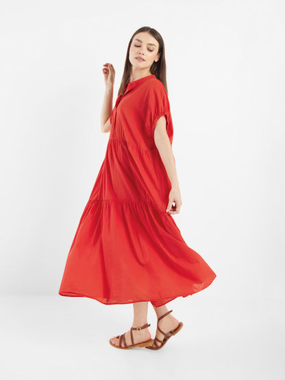 Eine Frau modelliert das Dress Cowboy Boho Red - ein knöchellanges, locker sitzendes rotes Kleid mit kurzen Ärmeln - mit braunen flachen Sandalen und steht vor einem einfarbig weißen Hintergrund, wobei sie leicht zur Seite blickt.