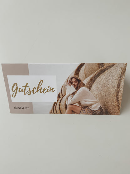 Eine Geschenkgutschein-Karte mit dem Wort "Gutschein" und einer Frau in einem hellen Pullover auf Heuballen vor weißem Hintergrund - eine stilvolle Mode-Geschenkidee.