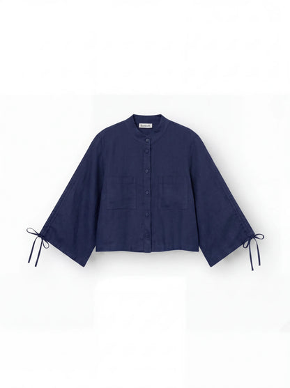 Die Bluse „Mary Linen Navy“ ist eine langärmelige Leinenbluse für Damen mit Stehkragen, zwei Brusttaschen, weiten Ärmeln mit Bindebündchen und einer verkürzten, kastenförmigen Passform in Marineblau. Dargestellt vor weißem Hintergrund.