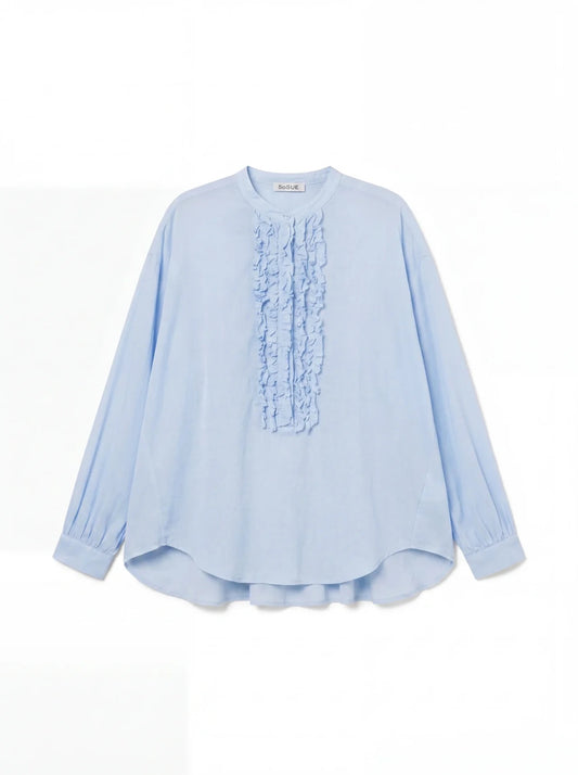 Die Bluse Bruna Light Blue ist eine langärmelige Sommerbluse mit Rundhalsausschnitt, gerüschten Details auf der Vorderseite, geknöpften Manschetten und einer lockeren Passform aus weichem Baumwoll-Voile.