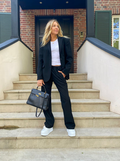 Eine Frau in Anzug und Hose Karoline Black steht selbstbewusst auf der Treppe und verkörpert perfekt ein stilvolles Businessoutfit Damen.