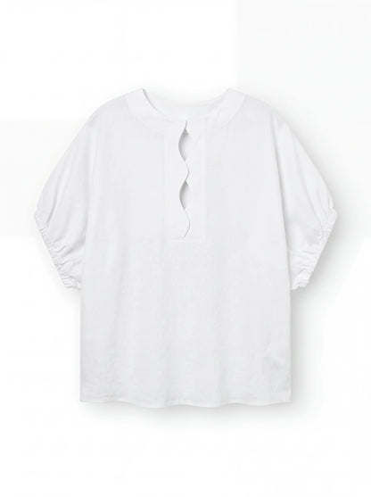 Die Bluse Cowboy Wave Linen White ist eine locker sitzende weiße Leinenbluse mit ellenbogenlangen gerafften Ärmeln, einem überschnittenen Schlüssellochausschnitt im Rücken und dezenten Wellendetail-Akzenten.