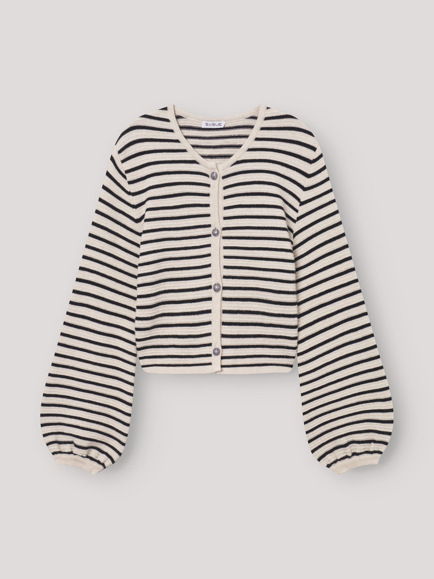 Jacke Fiene ist eine cremefarbene, kurz geschnittene maritime Strickjacke mit schwarzen Streifen, Knöpfen vorne, leicht gepufften langen Ärmeln mit gerafften Bündchen und rundem Halsausschnitt. Sie liegt flach auf einem hellen Untergrund.