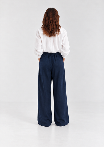 Eine Person, von hinten gesehen, die ein weißes Hemd trägt, das in eine weit geschnittene Hose Josy Linen Navy gesteckt ist.