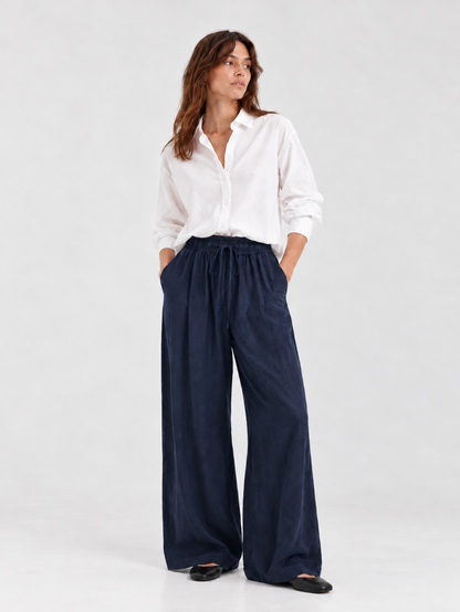 Frau, die ein weißes, langärmeliges Hemd mit Knöpfen und die Hose Josy Linen Navy trägt – eine hoch taillierte Hose mit weitem Bein und Kordelzug in der Taille.