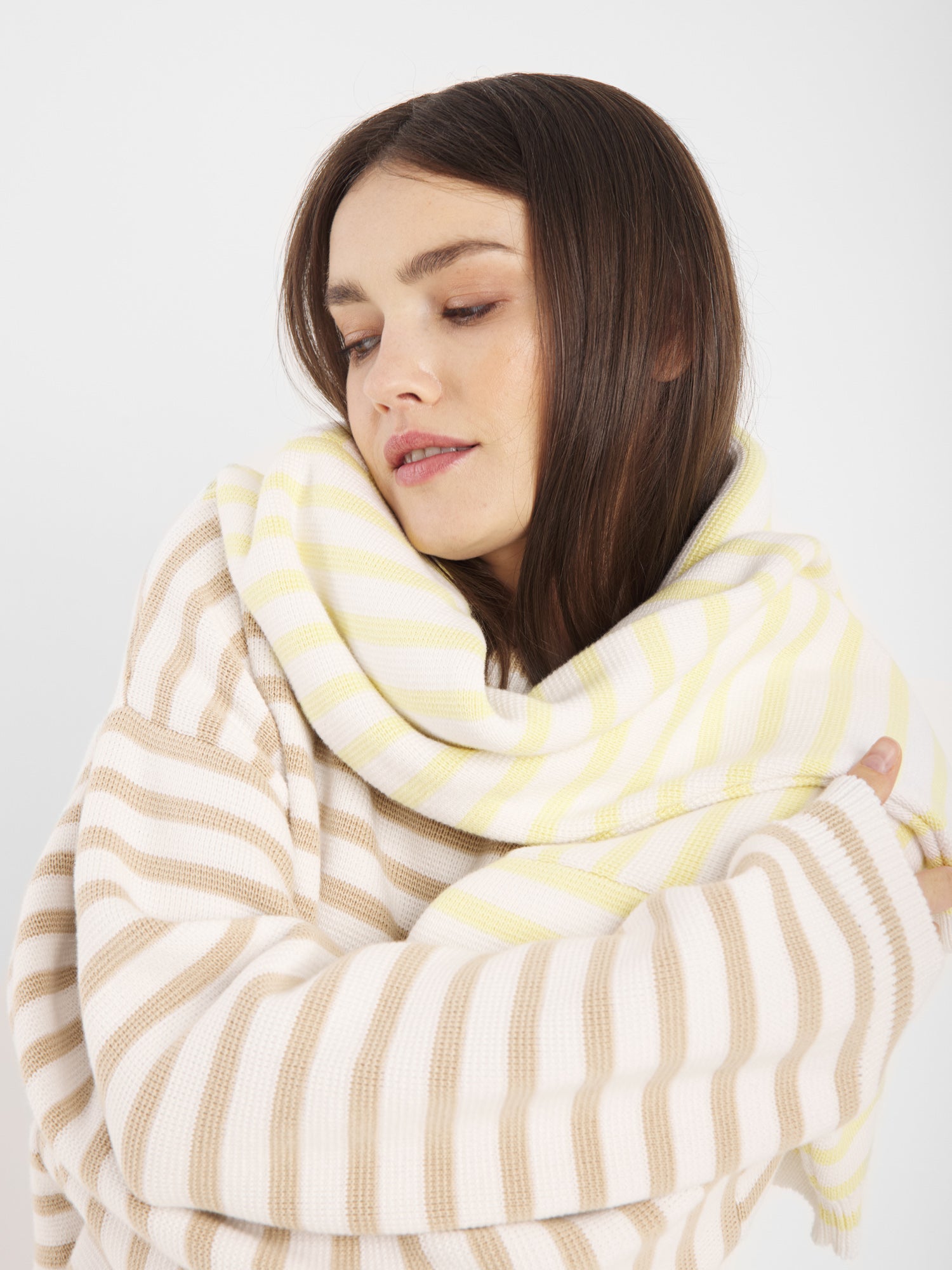 Eine Frau mit langen braunen Haaren trägt den Pullover Sailor Beige Offwhite und blickt gelassen auf einen schlichten weißen Hintergrund.