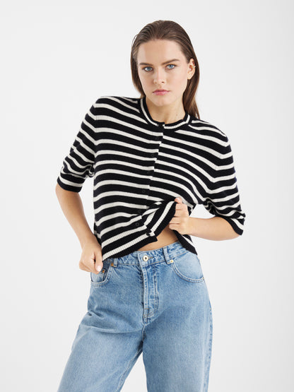 Eine Person mit langen braunen Haaren trägt die Sailor Jacket Short Blue White Stripes und hellblaue Jeans mit hoher Taille, steht vor einem schlichten weißen Hintergrund und blickt selbstbewusst in die Kamera.