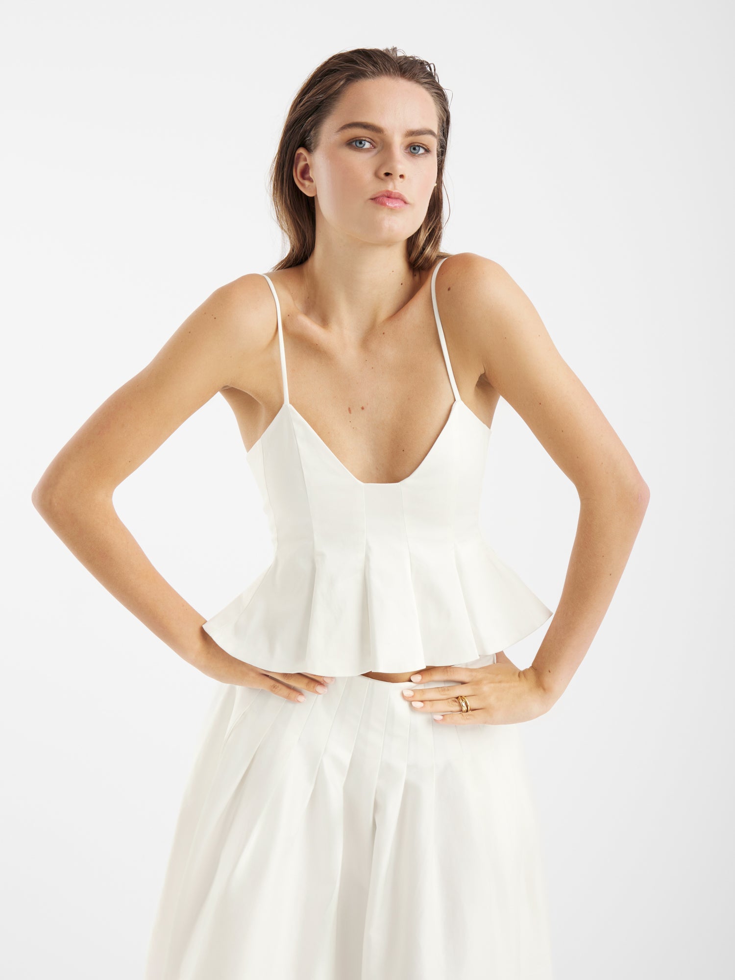 Eine Frau im Top Audrey White und passendem Rock steht selbstbewusst mit den Händen auf den Hüften - ein perfektes Sommer-Essential für jede Trägertop Damen-Garderobe.