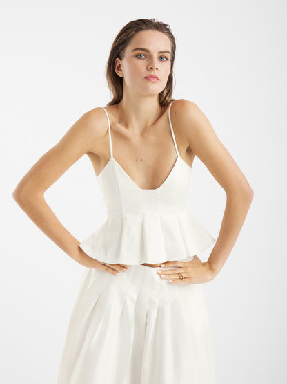 Eine Frau im Top Audrey White und passendem Rock steht selbstbewusst mit den Händen auf den Hüften - ein perfektes Sommer-Essential für jede Trägertop Damen-Garderobe.