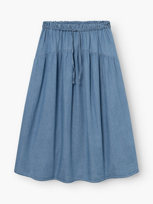 Der Rock Palma Denim ist ein knielanger, hellblauer Jeansrock mit elastischem Bund, Kordelzug und leichten Falten, flach auf weißem Grund.