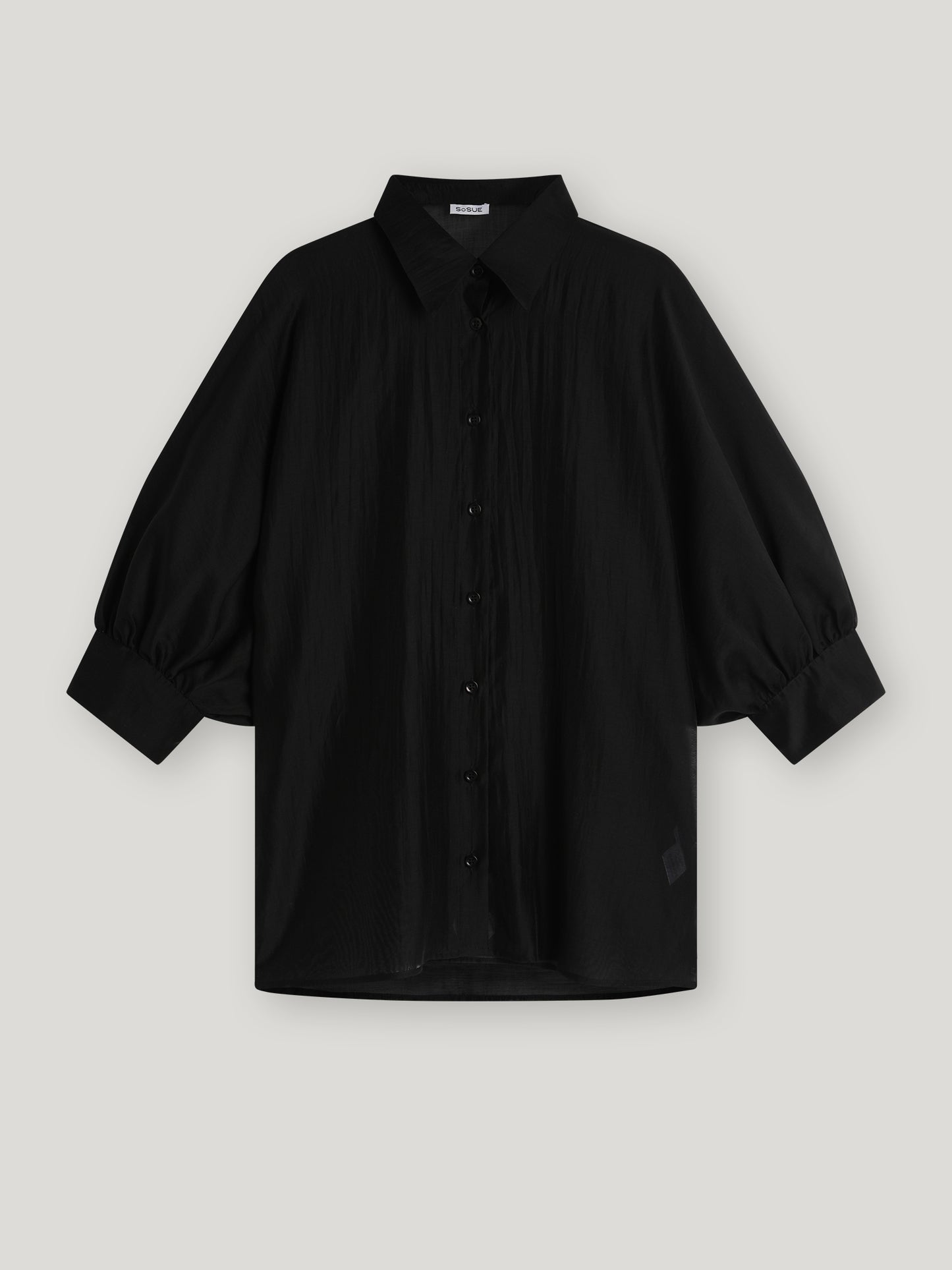 Die Bluse Antonia Short Sleeve Black ist eine locker sitzende schwarze Bluse mit Kragen, übergroßem Schnitt und weiten Dreiviertel-Ärmeln, die an den Manschetten gerafft sind, auf einem hellgrauen Hintergrund.