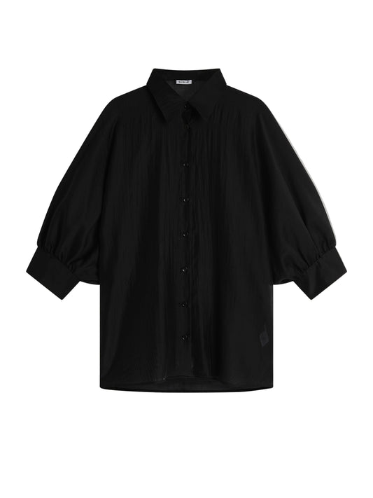 Die Bluse Antonia Short Sleeve Black ist eine locker sitzende schwarze Bluse mit Kragen, übergroßem Schnitt und weiten Dreiviertel-Ärmeln, die an den Manschetten gerafft sind, auf einem hellgrauen Hintergrund.