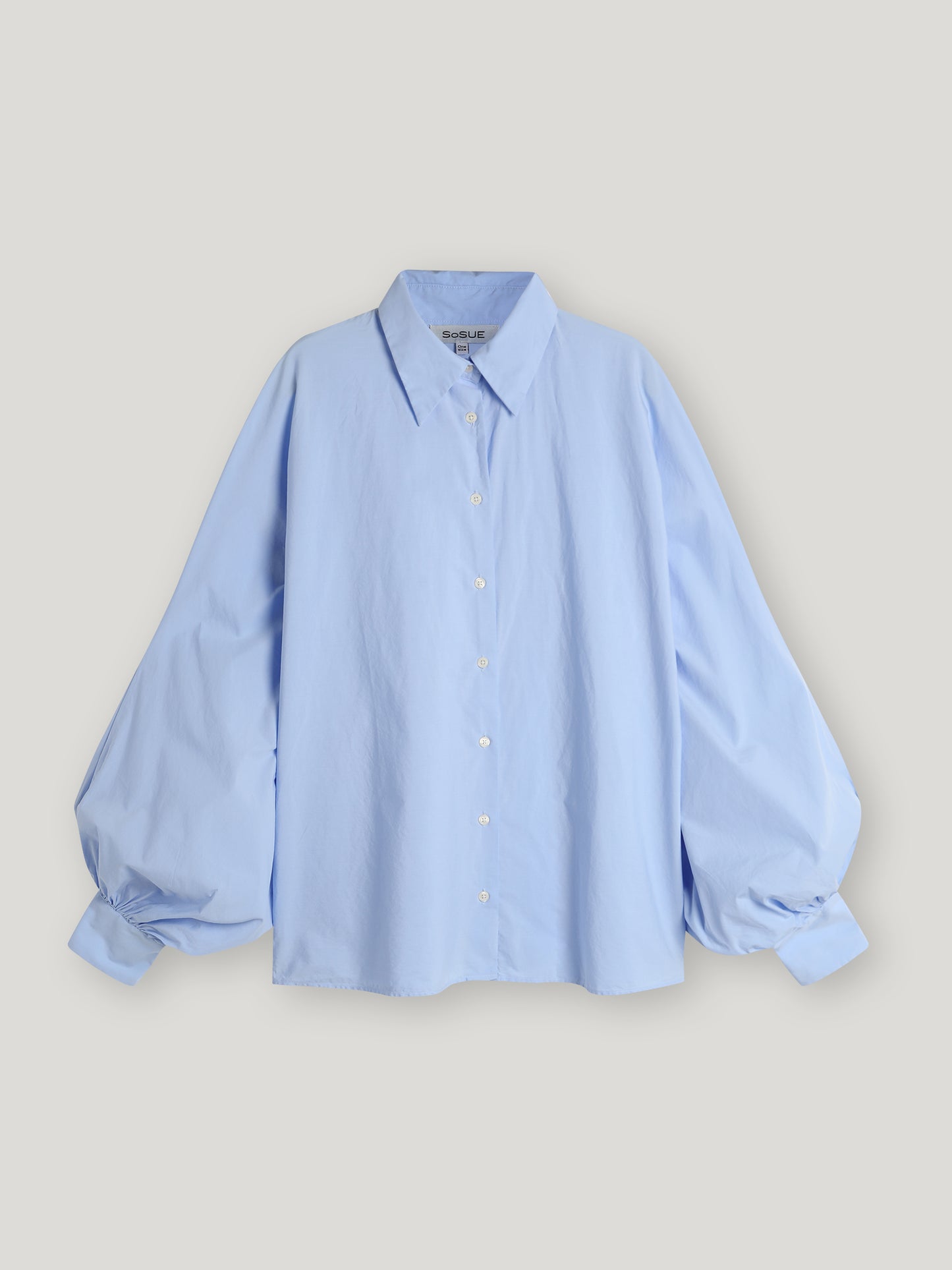 Die Bluse Antonia Lightblue ist eine übergroße Bluse mit einem Hemdblusenkragen und weiten Ärmeln, die vor einem schlichten hellen Hintergrund gezeigt wird.