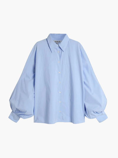 Die Bluse Antonia Lightblue ist eine hellblaue Baumwollbluse mit Kragen und voluminösen Ballonärmeln in One Size, stilvoll präsentiert auf schlichtem, weißem Hintergrund.