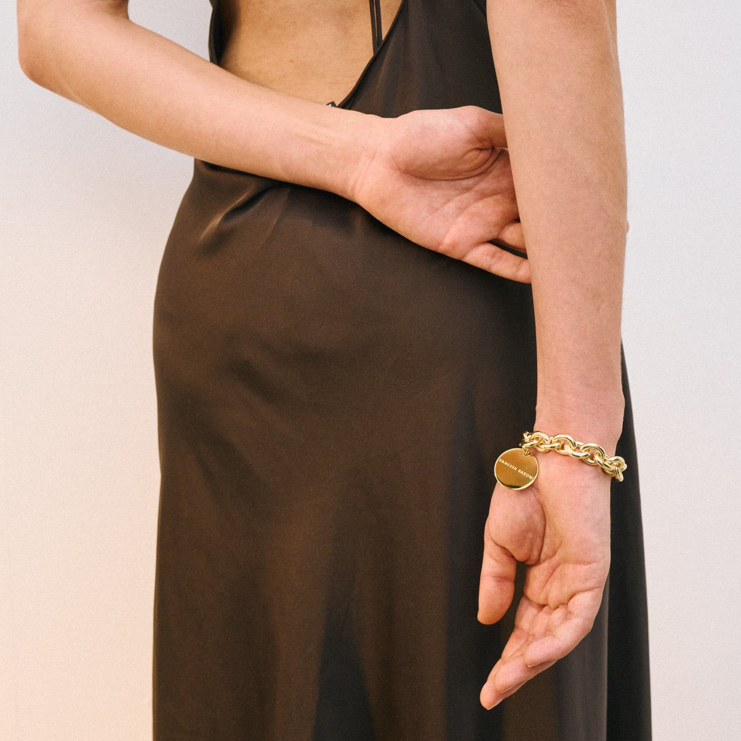 Eine Person in einem ärmellosen, rückenfreien Kleid aus dunklem Satin steht mit einem Arm hinter dem Rücken und präsentiert das klobige Vanessa Baroni x SOSUE Bracelet Gold - ein auffälliges Armband Damen.
