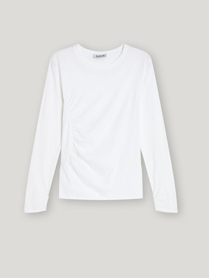 Das Shirt Gathering White ist ein Damen Langarmshirt aus nachhaltiger Baumwolle mit rundem Ausschnitt und dezenter seitlicher Raffung, stilvoll präsentiert vor hellgrauem Hintergrund.