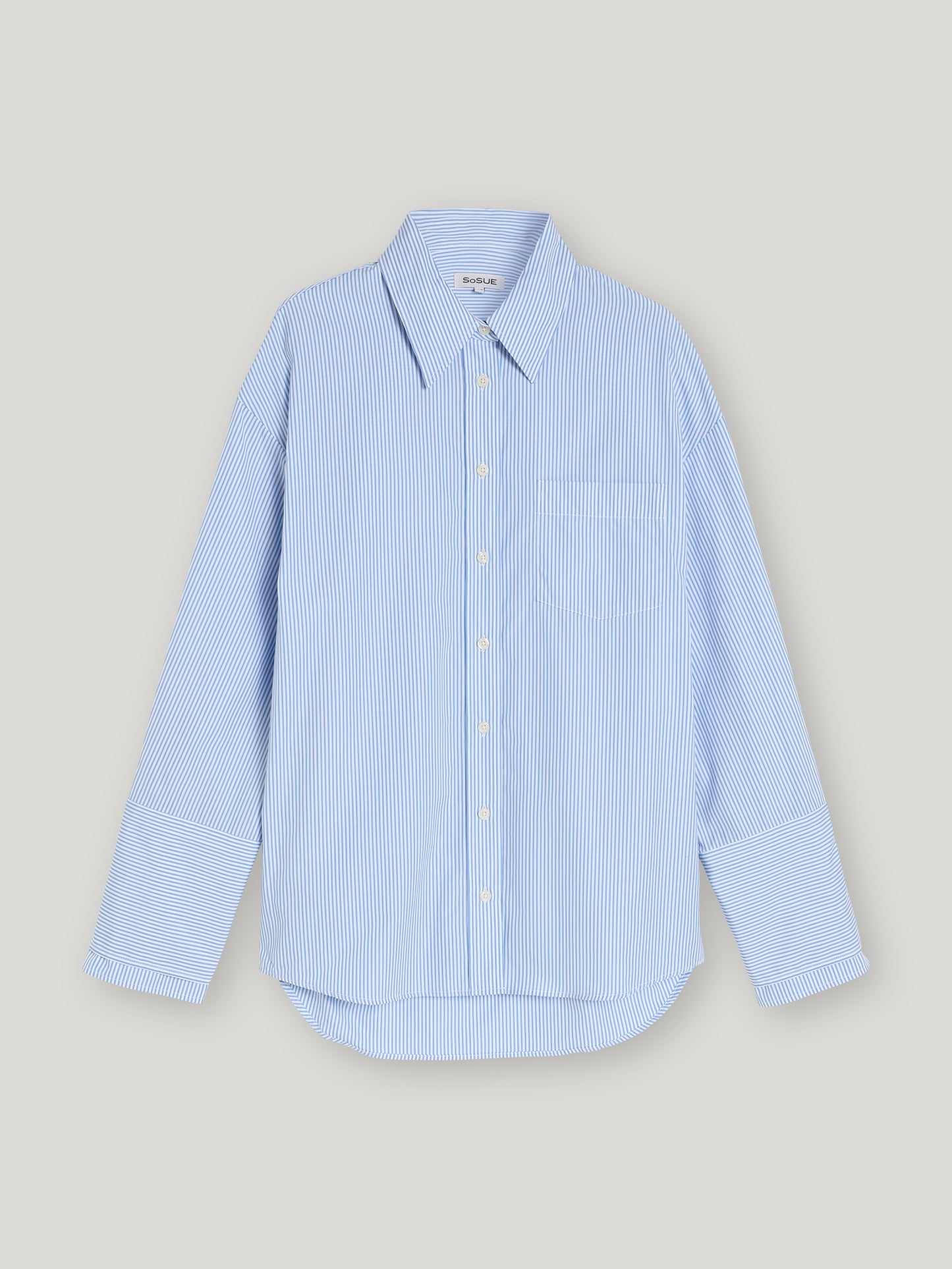 Die Bluse Malin Stripe ist eine Damenbluse mit blau-weißen Streifen, langem Arm, spitzem Kragen, Brusttasche und weißen Knöpfen. Sie wird vor einem schlichten hellgrauen Hintergrund präsentiert.