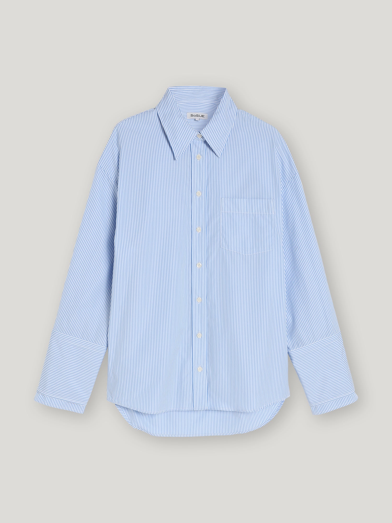 Die Bluse Malin Stripe ist eine Damenbluse mit blau-weißen Streifen, langem Arm, spitzem Kragen, Brusttasche und weißen Knöpfen. Sie wird vor einem schlichten hellgrauen Hintergrund präsentiert.