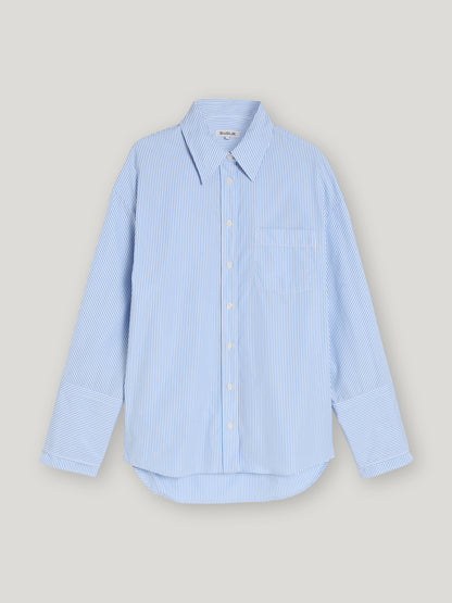 Die Bluse Malin Stripe ist eine Damenbluse mit blau-weißen Streifen, langem Arm, spitzem Kragen, Brusttasche und weißen Knöpfen. Sie wird vor einem schlichten hellgrauen Hintergrund präsentiert.