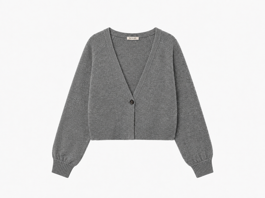 Der kurze Cardigan „Antonia“ in Grau ist ein kurz geschnittener Damen-Cardigan mit langen Ärmeln aus feinem Strick, einem tiefen V-Ausschnitt und einem einzelnen Knopfverschluss vorne, der sorgfältig auf weißem Hintergrund angeordnet ist.
