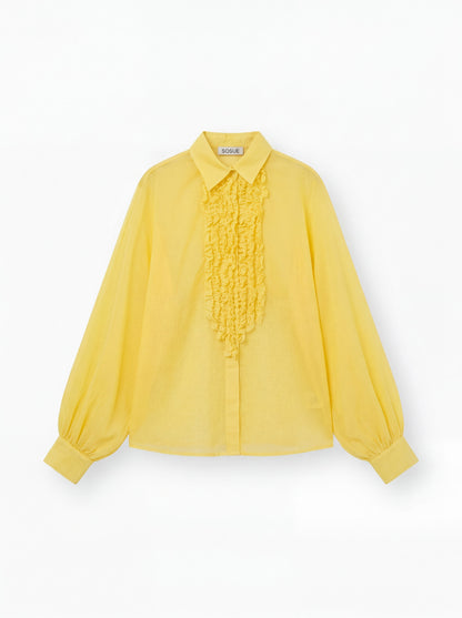 Die gelbe Bluse Antonia Slim Ruffle hat lange Ärmel, einen spitzen Kragen, eine geknöpfte Vorderseite, eine gerüschte Brustpartie und lose geraffte Manschetten. Das SOUGE Label ist auf der Innenseite des Kragens sichtbar.