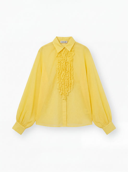 Die gelbe Bluse Antonia Slim Ruffle hat lange Ärmel, einen spitzen Kragen, eine geknöpfte Vorderseite, eine gerüschte Brustpartie und lose geraffte Manschetten. Das SOUGE Label ist auf der Innenseite des Kragens sichtbar.