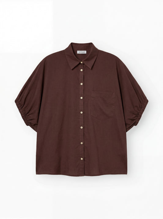 Das Cowboy Collar Voile Brown ist ein locker sitzendes, braunes Hemd zum Knöpfen mit Kragen, kurzen Puffärmeln, die an den Manschetten gerafft sind, und einer einzelnen Brusttasche, abgebildet auf einem schlichten weißen Hintergrund.