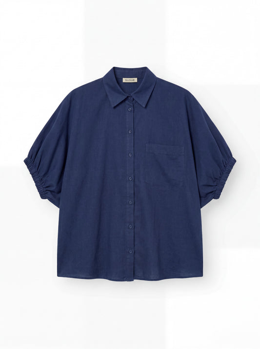 Das Cowboy Collar Voile Navy ist ein locker sitzendes, kurzärmeliges, marineblaues Button-up-Hemd mit einer einzigen Brusttasche und gerafften Ärmeln, das auf einem einfarbig weißen Hintergrund abgebildet ist.
