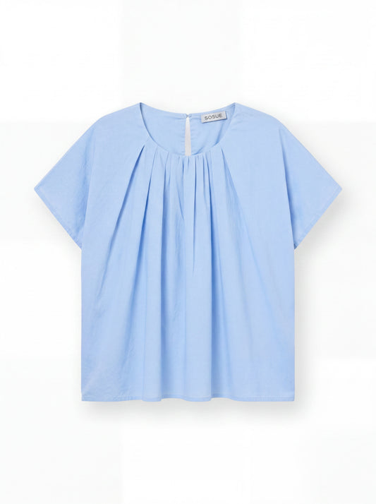 Die Bluse Tulip Light Blue ist eine hellblaue, leichte Baumwollbluse mit kurzen Ärmeln, Rundhalsausschnitt, Frontfalten und kleinem Knopfverschluss am Rücken - präsentiert auf weißem Hintergrund.