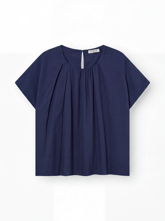 Die Bluse Tulip Navy ist eine kurzärmelige, dunkelblaue Damen Bluse mit Rundhalsausschnitt, plissierter Vorderseite, kleinem Schlüssellochknopf auf der Rückseite und lockerer Passform aus Baumwolle. Ausgestellt auf weißem Hintergrund.