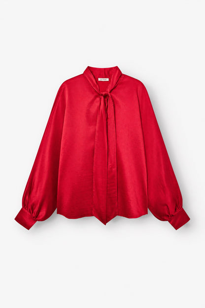 Bluse „Antonia Bow Red“: Eine leuchtend rote, langärmelige Bluse mit Ballonärmeln, geknöpften Manschetten, lockerer Passform und hohem Ausschnitt, verziert mit einer großen Schleife vorne, abgebildet vor weißem Hintergrund.