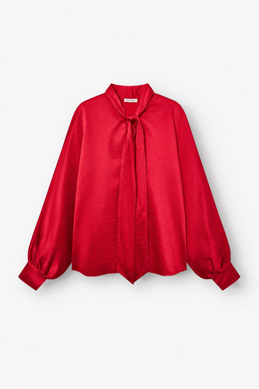 Bluse „Antonia Bow Red“ aus leuchtend rotem Satin mit langen, weit fallenden Ärmeln, lockerer Passform, geknöpften Ärmelbündchen und einer auffälligen Schleife am Hals, abgebildet vor weißem Hintergrund.