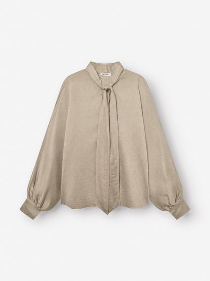 Bluse „Antonia Bow“ in Taupe: Eine beigefarbene, langärmelige Bluse mit lockerer Passform, die sich durch einen Bindegürtel am Halsausschnitt und breite Manschetten auszeichnet und vor weißem Hintergrund präsentiert wird.
