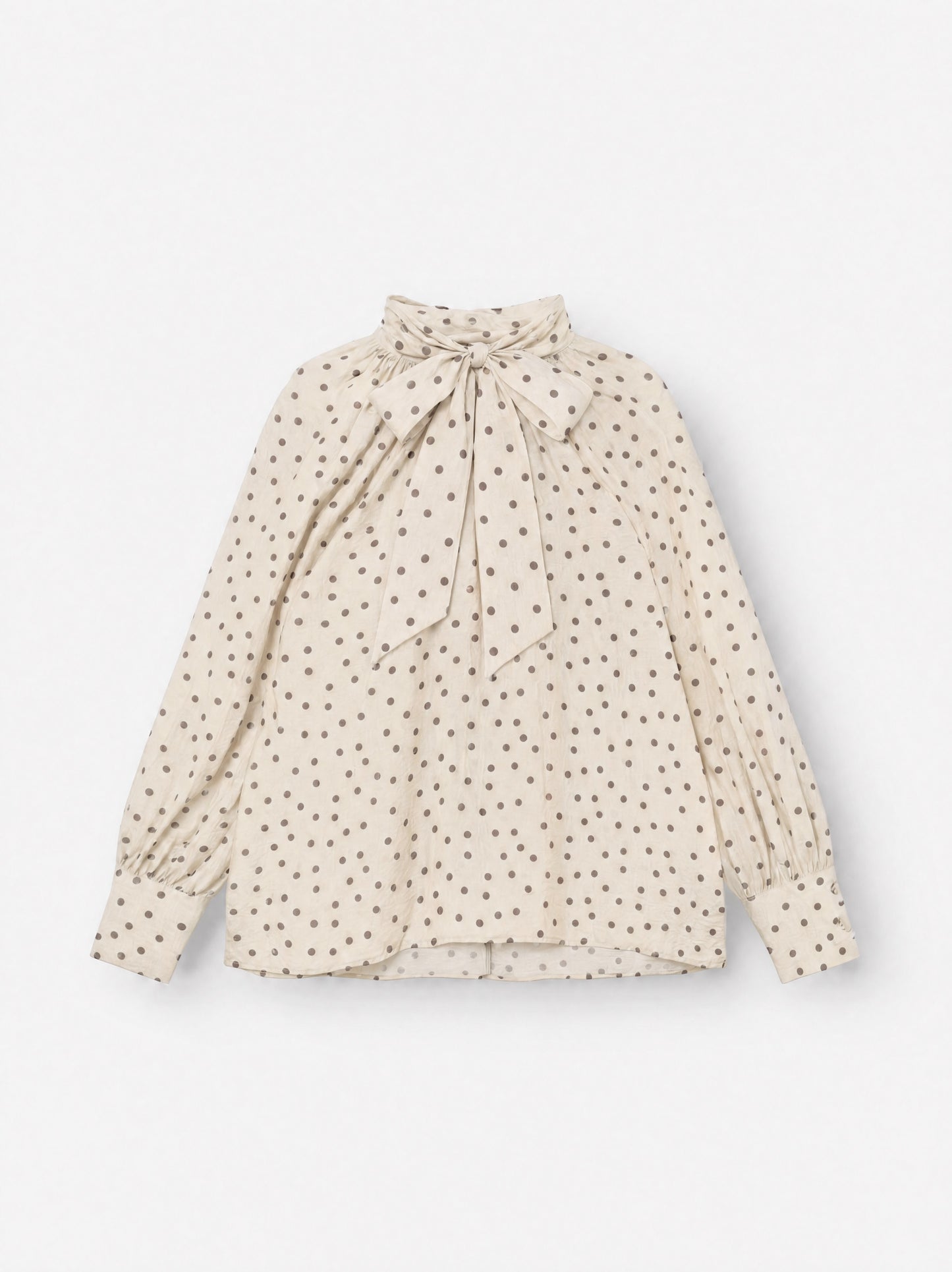 Die Bluse „Dotty Bow Ecru Brown“ ist eine langärmelige Bluse mit braunen Polka-Punkten, einem hohen Ausschnitt und einer übergroßen Schleife, die am Hals gebunden wird. Sie wurde in Italien aus feinem Baumwoll-Voile gefertigt und verfügt über geknöpfte Ärmelbündchen sowie eine lockere, fließende Passform.