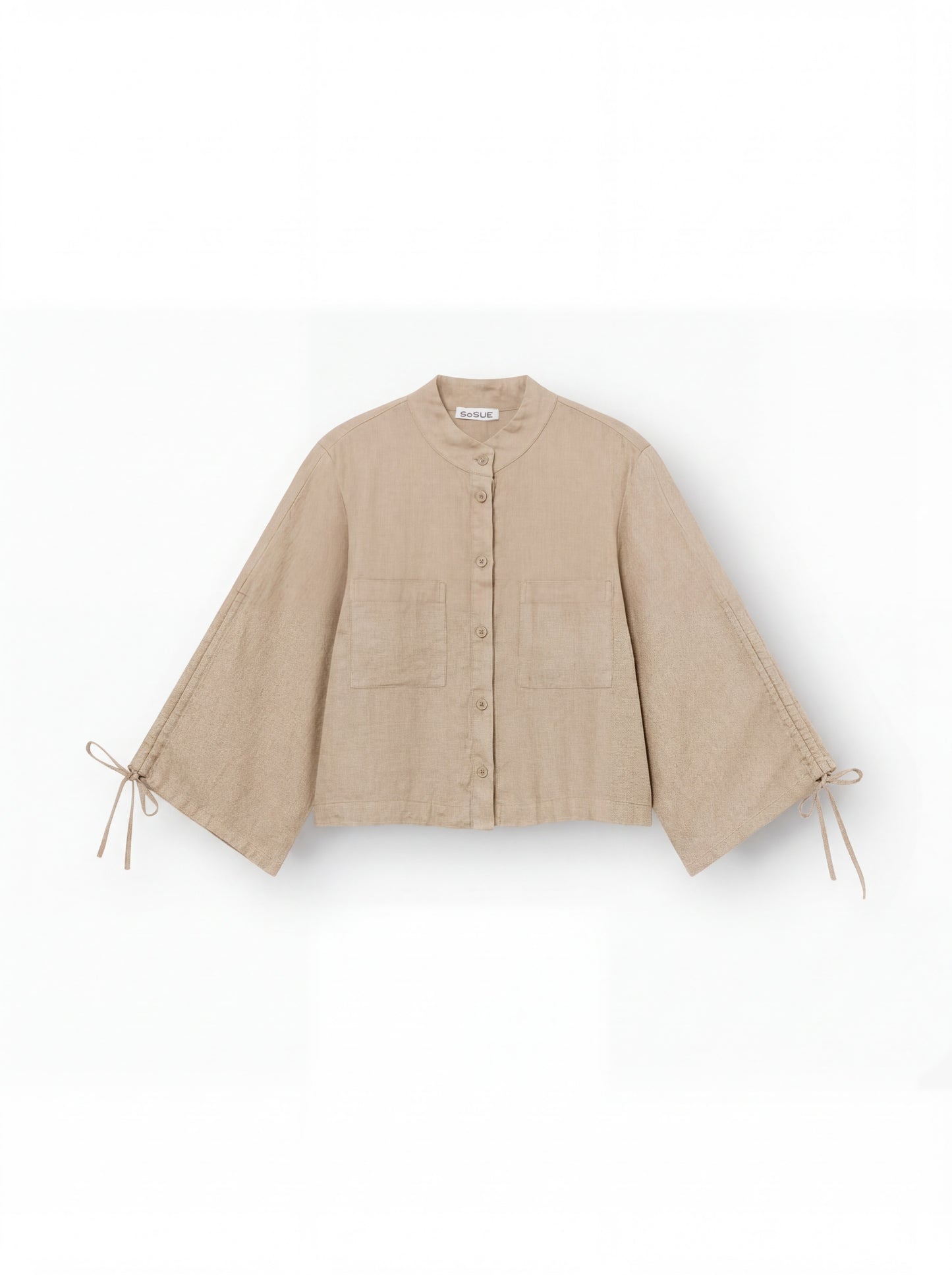 Die Bluse Mary Linen Beige ist eine beige Leinenbluse mit Knopfleiste, weitem Schnitt, verstellbaren Ärmeln samt Schleifendetails, Rundkragen und zwei aufgesetzten Fronttaschen.