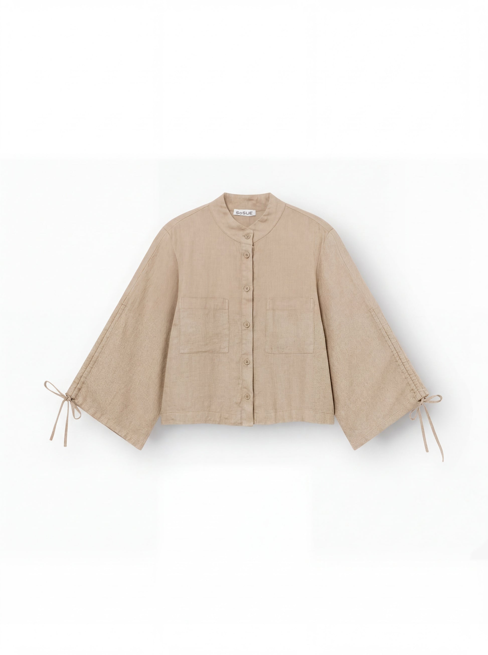 Die Bluse Mary Linen Beige ist eine beige Leinenbluse mit Knopfleiste, weitem Schnitt, verstellbaren Ärmeln samt Schleifendetails, Rundkragen und zwei aufgesetzten Fronttaschen.