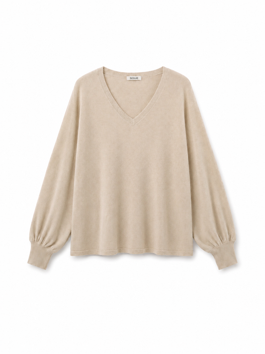 Der Pullover „Antonia“ mit V-Ausschnitt in der Farbe „Powder“ (Beige) wird vor einem weißen Hintergrund präsentiert. Er verfügt über lange Ärmel, eine lockere Passform und elegante Ballonärmel. Dieser Pullover aus Merinowolle verbindet zeitlosen Stil mit außergewöhnlichem Tragekomfort.