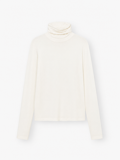 Das „Turtle Jersey White“, ein schlichter, langärmeliger, cremefarbener Rollkragenpullover, wird vor weißem Hintergrund präsentiert – ideal als weißes Jersey-Shirt für jeden Anlass. Dieses stilvolle Rollkragen-Shirt für Damen wird in Portugal meisterhaft gefertigt und verbindet Komfort mit zeitloser Eleganz.