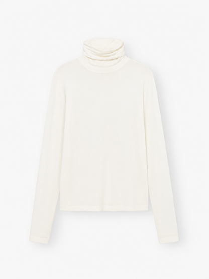 Das „Turtle Jersey White“, ein schlichter, langärmeliger, cremefarbener Rollkragenpullover, wird vor weißem Hintergrund präsentiert – ideal als weißes Jersey-Shirt für jeden Anlass. Dieses stilvolle Rollkragen-Shirt für Damen wird in Portugal meisterhaft gefertigt und verbindet Komfort mit zeitloser Eleganz.
